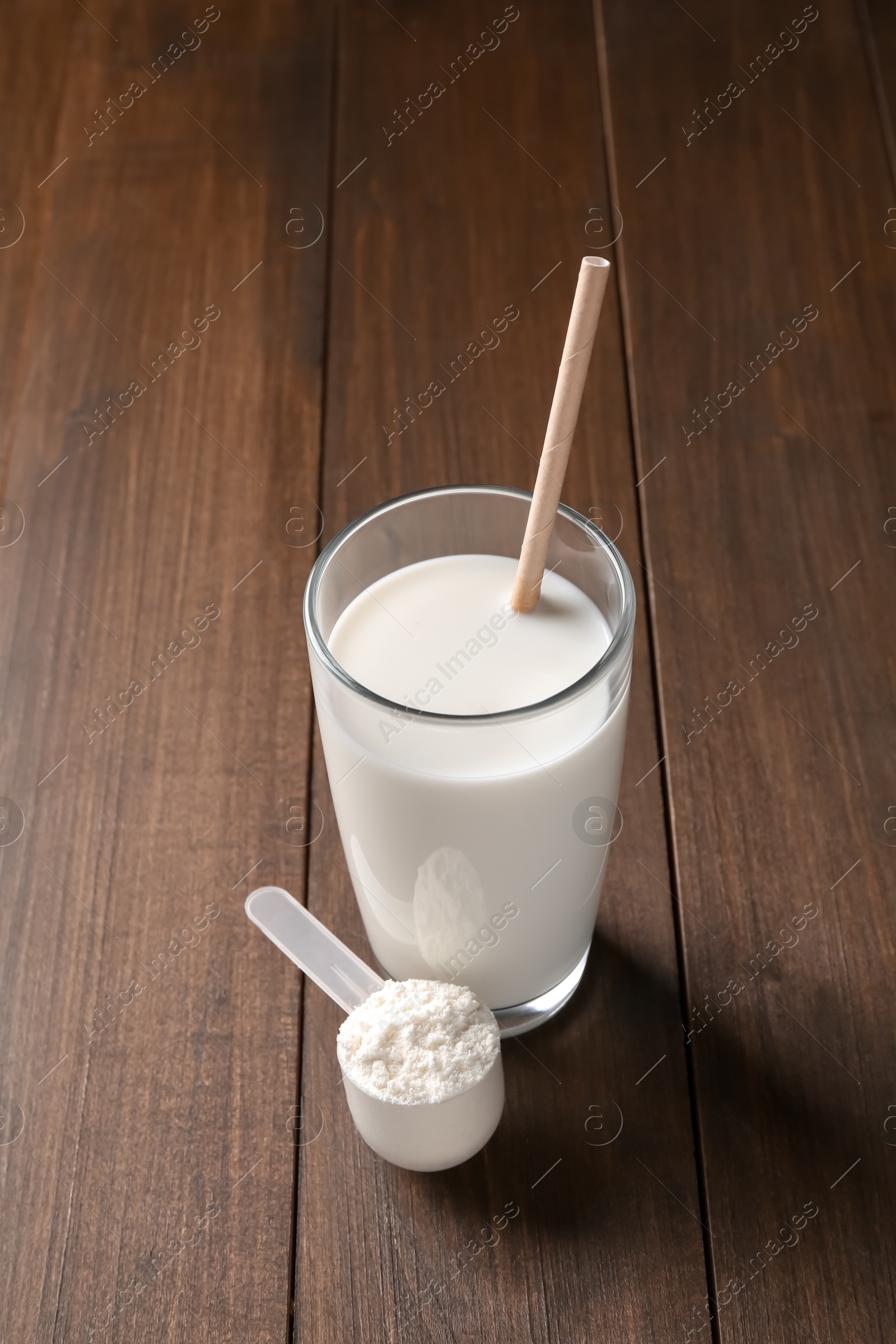 Photo of Delicious protein shake in glass and scoop with powder on wooden table