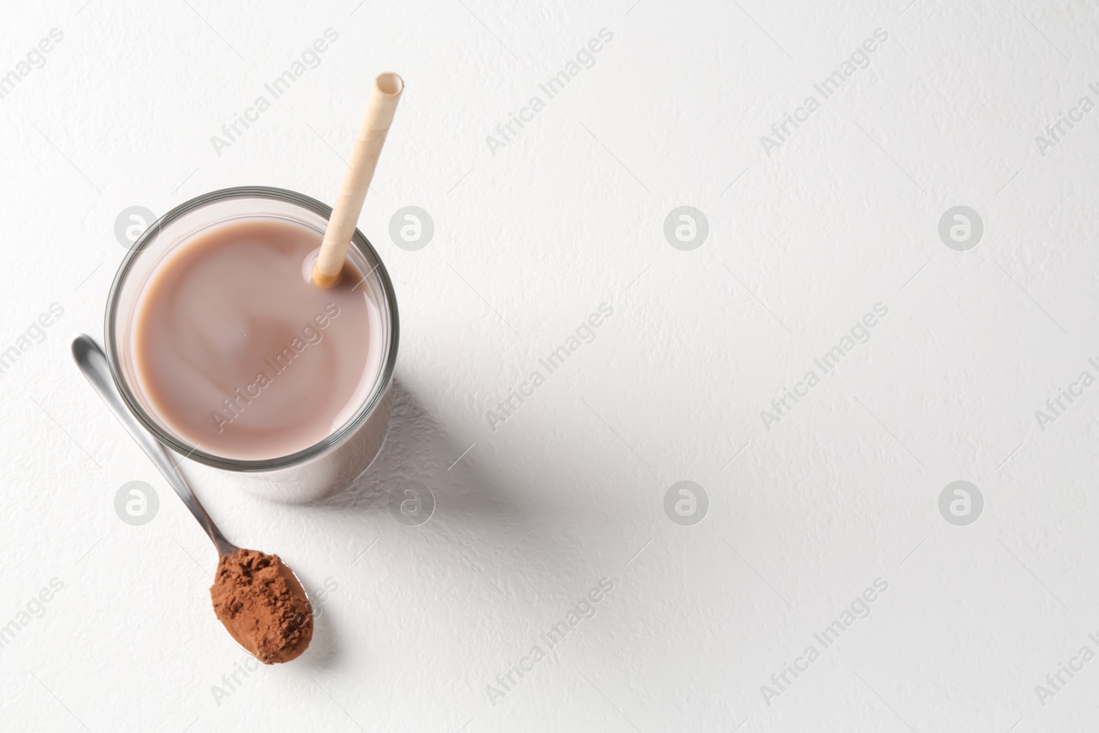 Photo of Delicious protein shake in glass and spoon with powder on white background, top view. Space for text