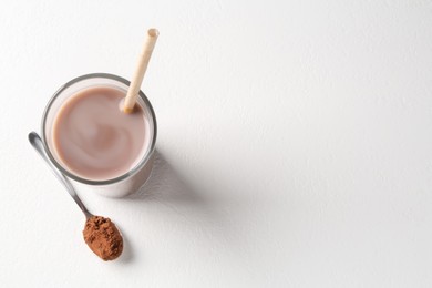 Photo of Delicious protein shake in glass and spoon with powder on white background, top view. Space for text