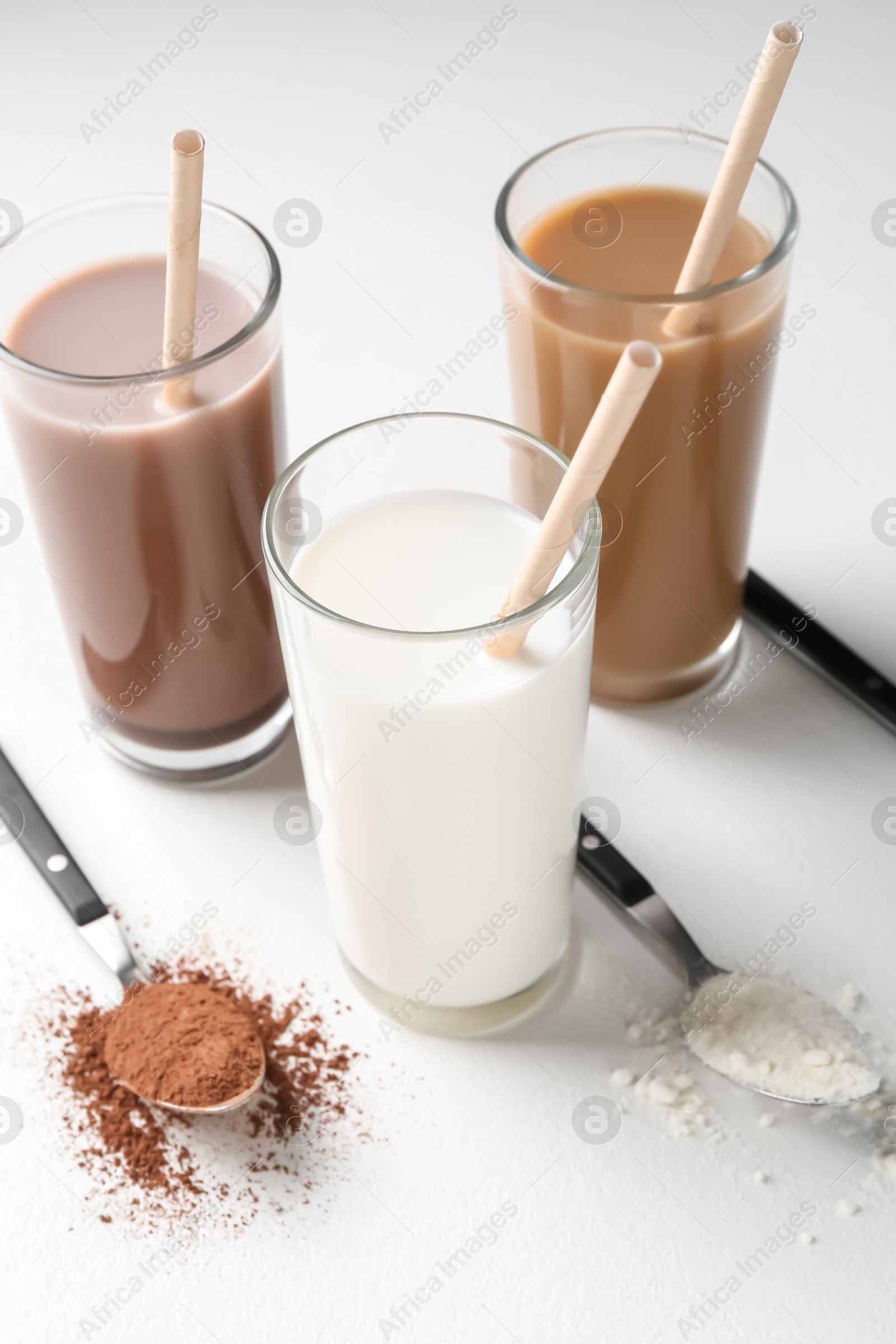 Photo of Delicious protein shakes in glasses and spoons with powder on white background