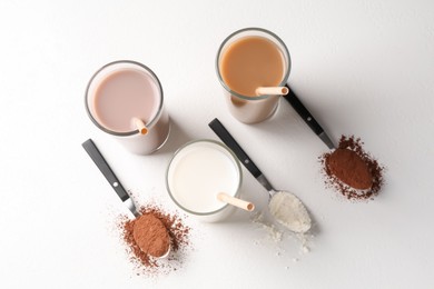 Photo of Delicious protein shakes in glasses and spoons with powder on white background, flat lay