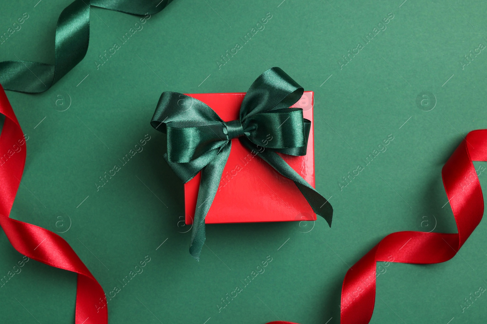 Photo of Beautiful red gift box with bright bow and ribbons on green background, flat lay