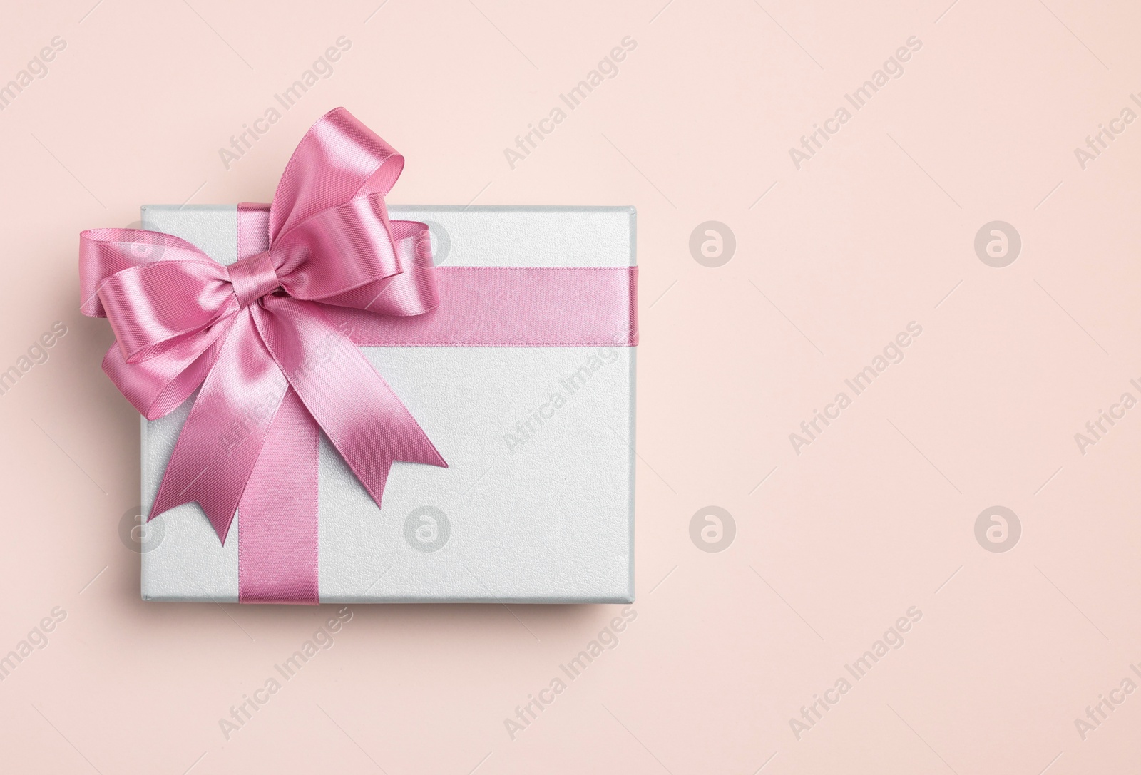 Photo of Beautiful gift box with pink bow on beige background, top view. Space for text