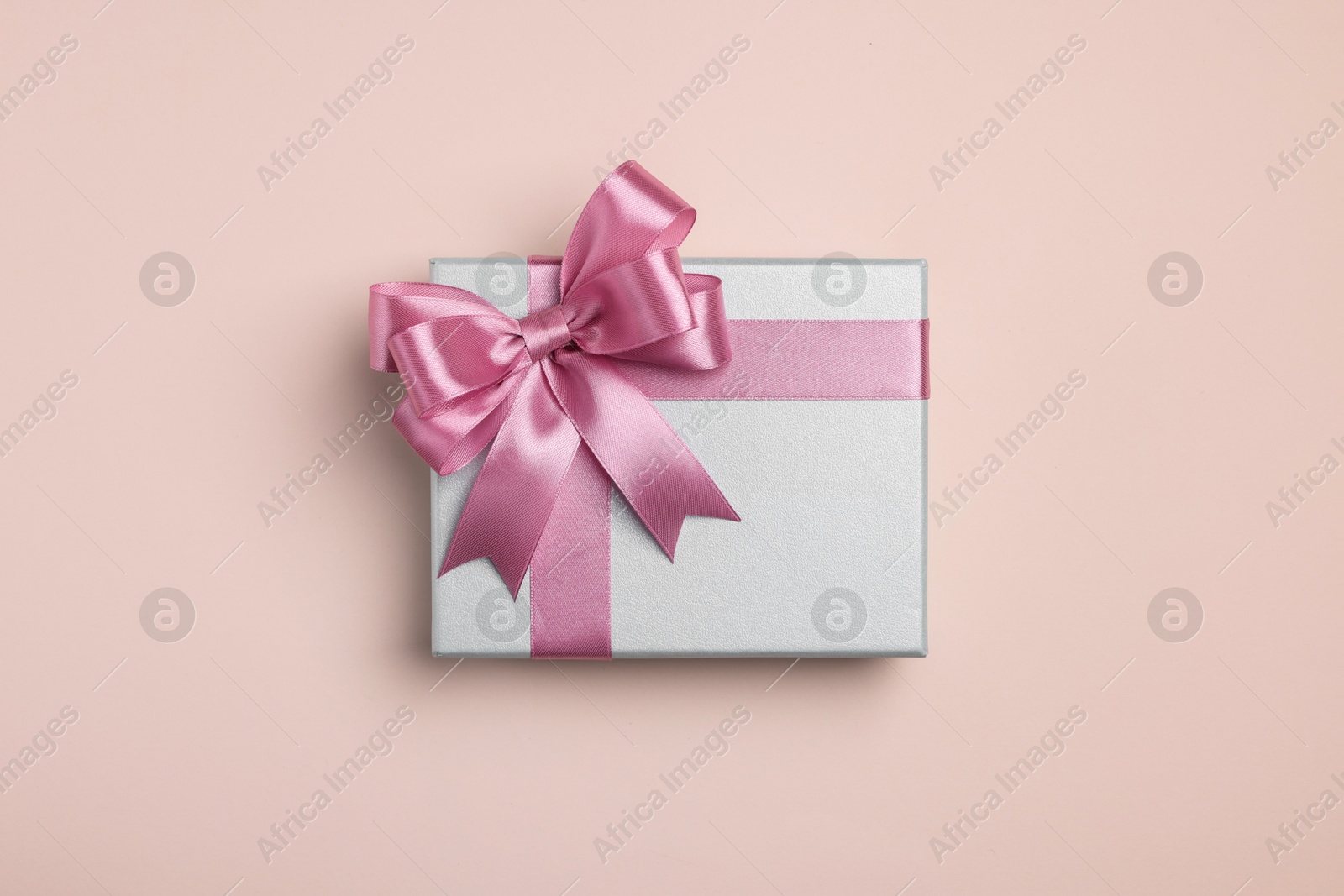 Photo of Beautiful gift box with pink bow on beige background, top view