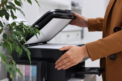 Photo of Woman using modern printer at workplace indoors, closeup