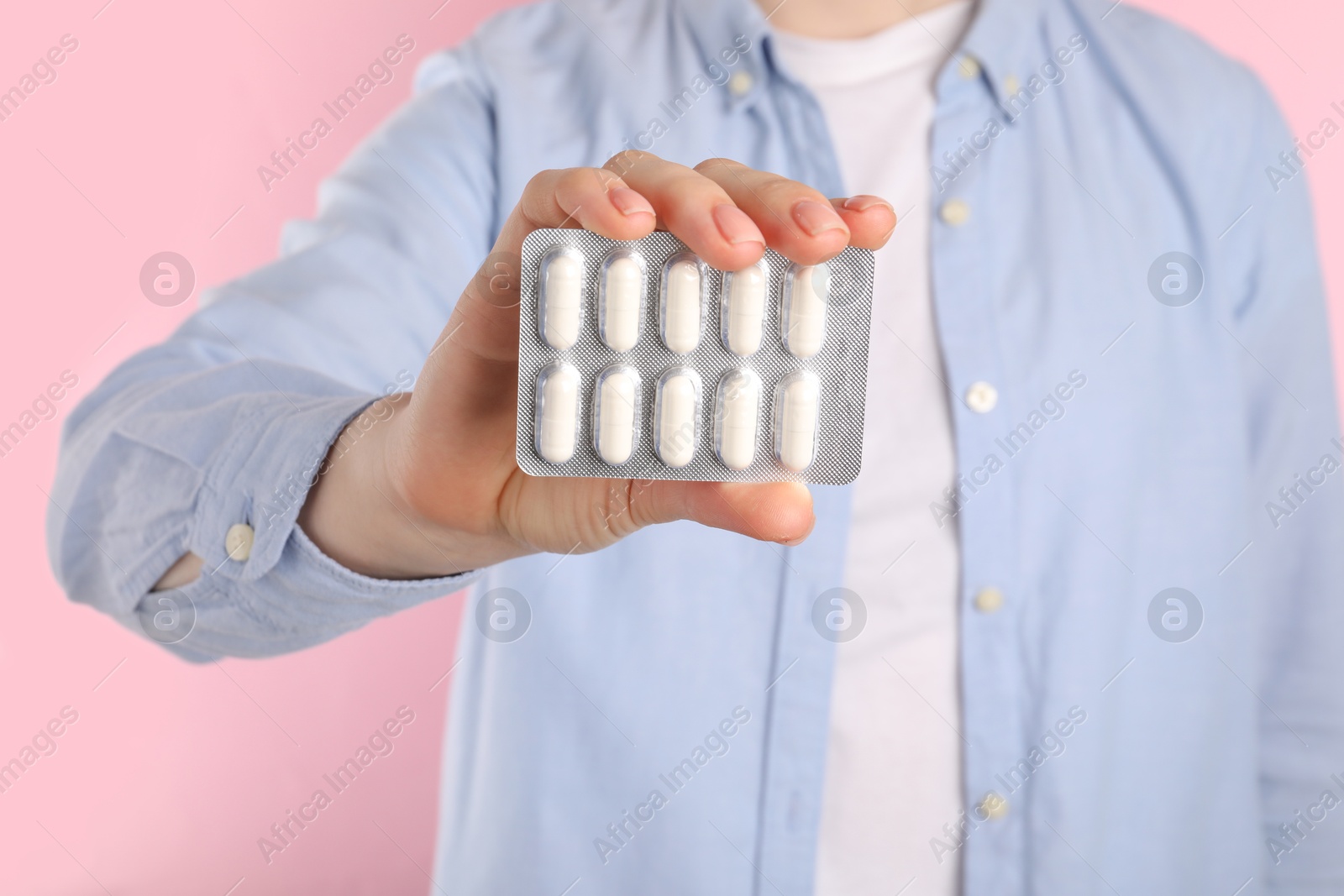 Photo of Woman holding blister with antibiotic pills on pink background, closeup