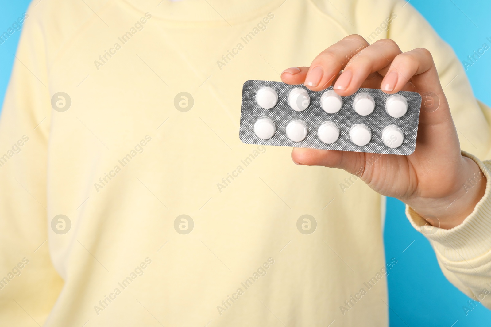 Photo of Woman holding blister with antibiotic pills on light blue background, closeup