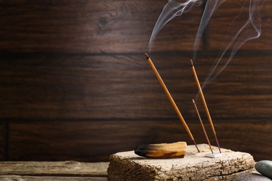 Photo of Aromatic incense sticks smoldering on wooden table. Space for text