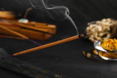 Photo of Aromatic incense stick smoldering in holder with om sign on black table, closeup