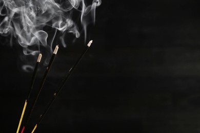 Photo of Aromatic incense sticks smoldering on black background, closeup. Space for text