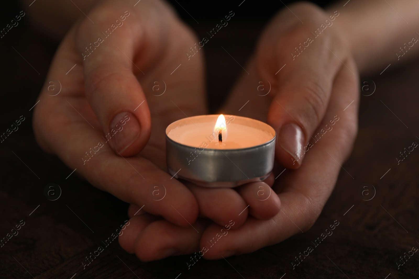 Photo of Woman holding burning tealight candle on black background, closeup