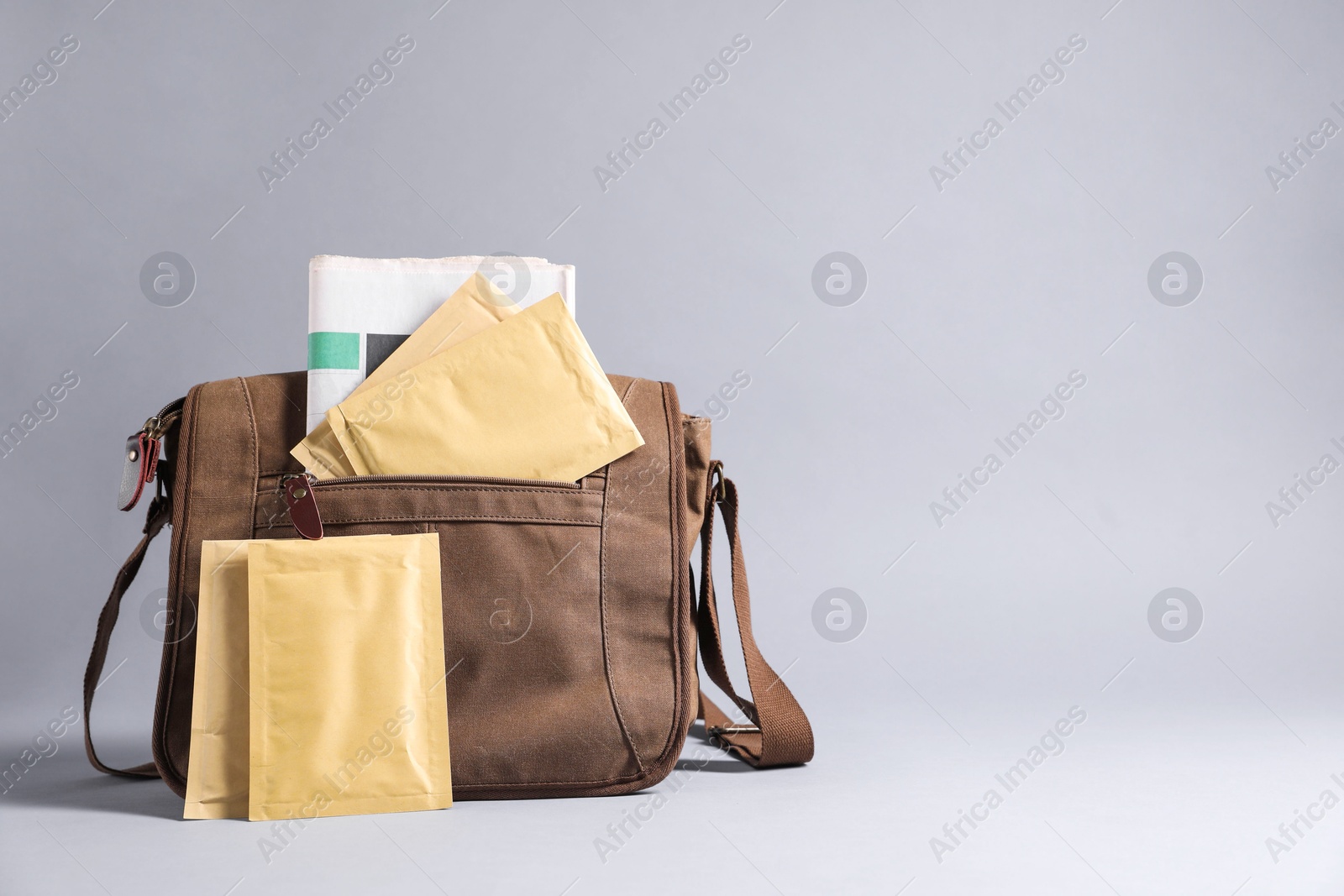 Photo of Brown postman's bag with envelopes and newspapers on grey background. Space for text