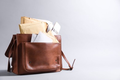 Photo of Brown postman's bag with envelopes and newspapers on grey background. Space for text