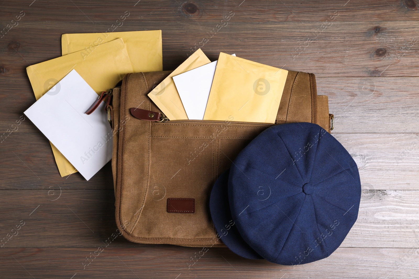 Photo of Brown postman's bag, envelopes, newspapers and hat on wooden table, top view