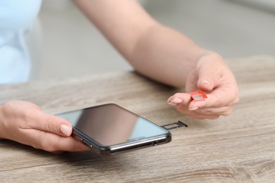 Woman holding SIM card and smartphone at wooden table indoors, closeup