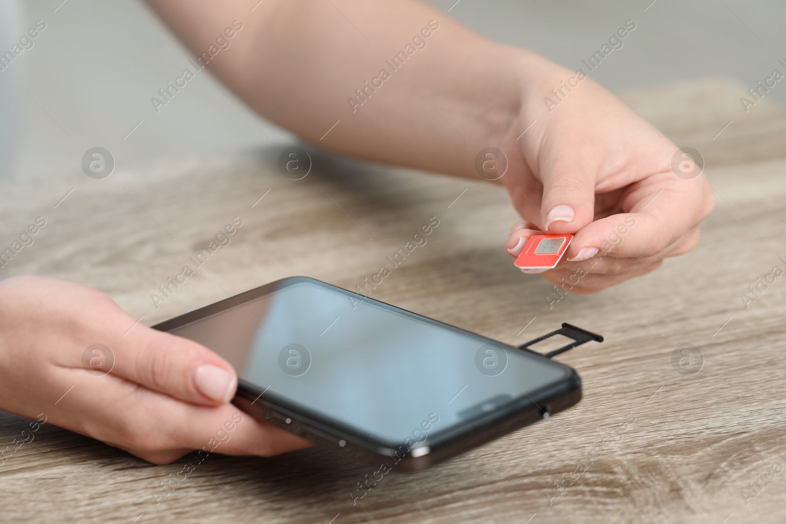 Photo of Woman holding SIM card and smartphone at wooden table indoors, closeup