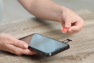 Woman holding SIM card and smartphone at wooden table indoors, closeup