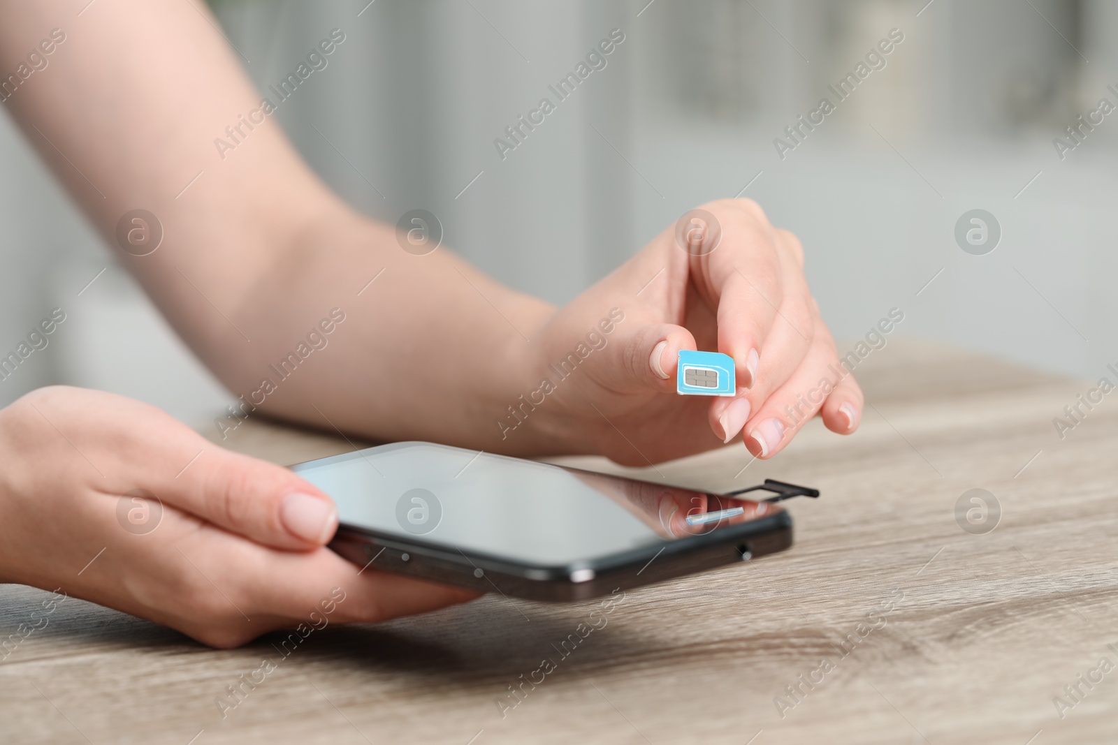 Photo of Woman holding SIM card and smartphone at wooden table indoors, closeup