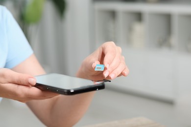 Woman holding SIM card and smartphone at home, closeup. Space for text