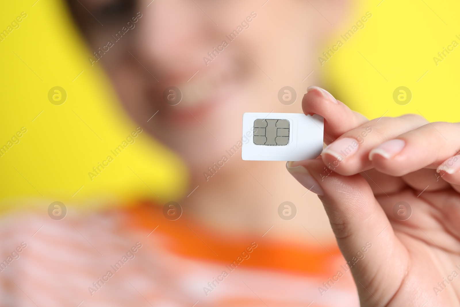 Photo of Woman holding SIM card on yellow background, closeup