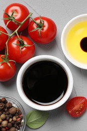 Photo of Balsamic vinegar, tomatoes, oil and peppercorns on light grey textured table, flat lay