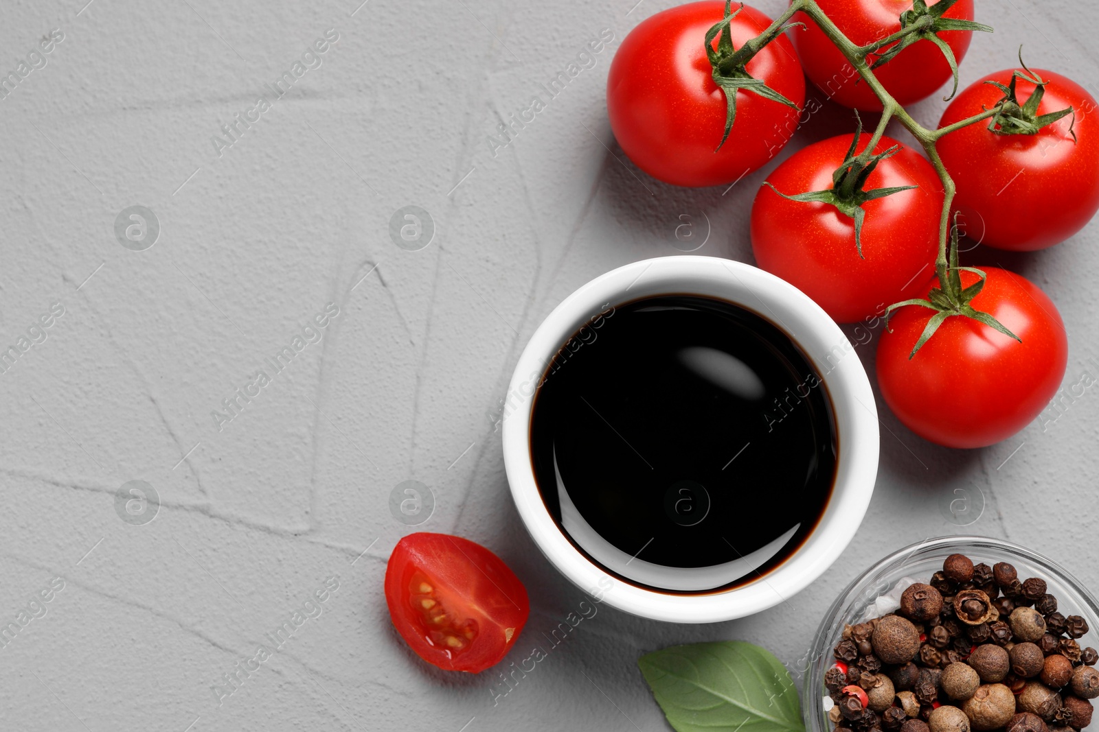 Photo of Balsamic vinegar, tomatoes and peppercorns on light grey textured table, flat lay. Space for text