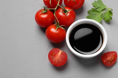 Photo of Balsamic vinegar, tomatoes and parsley on light grey textured table, flat lay. Space for text