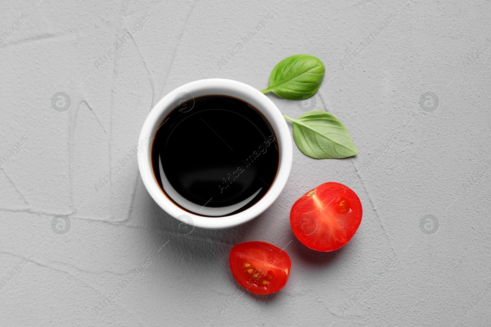 Photo of Balsamic vinegar, tomatoes and basil on light grey textured table, flat lay