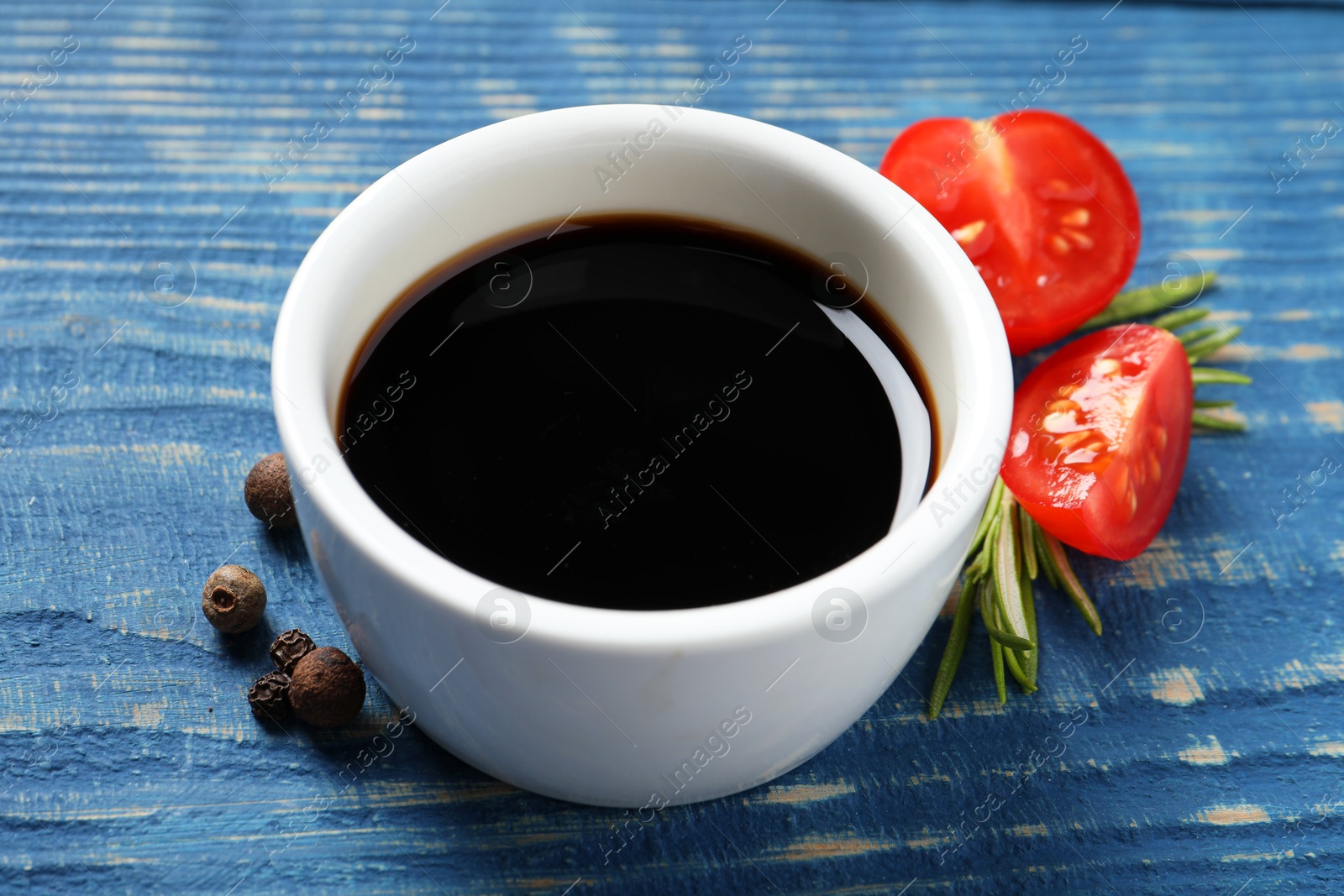 Photo of Balsamic vinegar, tomatoes, peppercorns and rosemary on blue wooden table, closeup