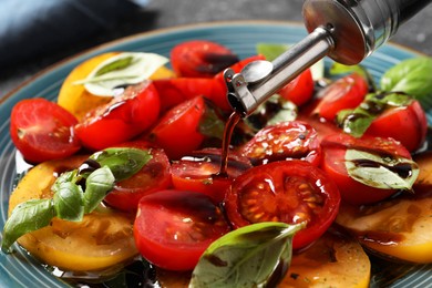 Pouring balsamic vinegar onto tasty salad on table, closeup