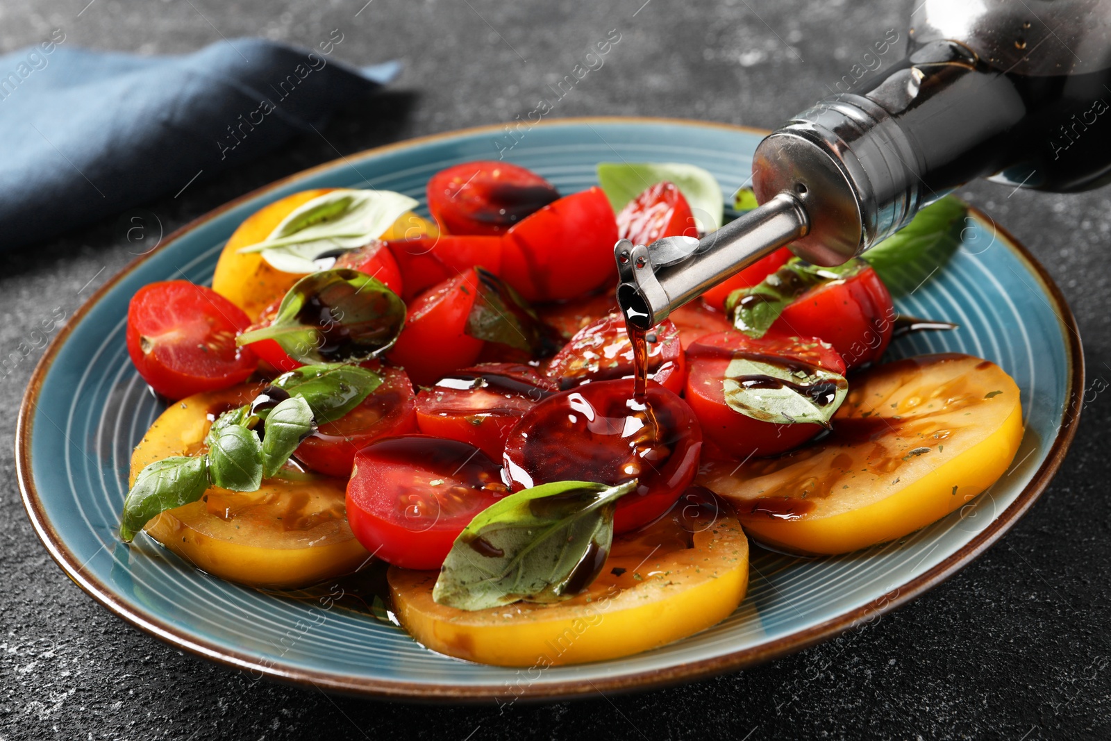 Photo of Pouring balsamic vinegar onto tasty salad on black textured table, closeup