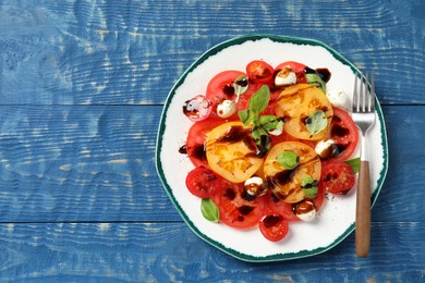 Photo of Tasty salad with balsamic vinegar, mozzarella and fork on blue wooden table, top view. Space for text