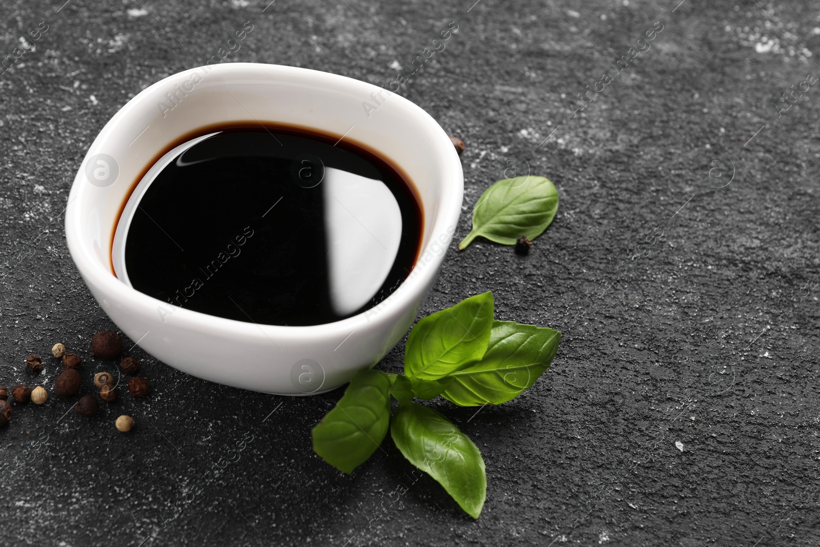 Photo of Balsamic vinegar, basil and peppercorns on black textured table, closeup. Space for text