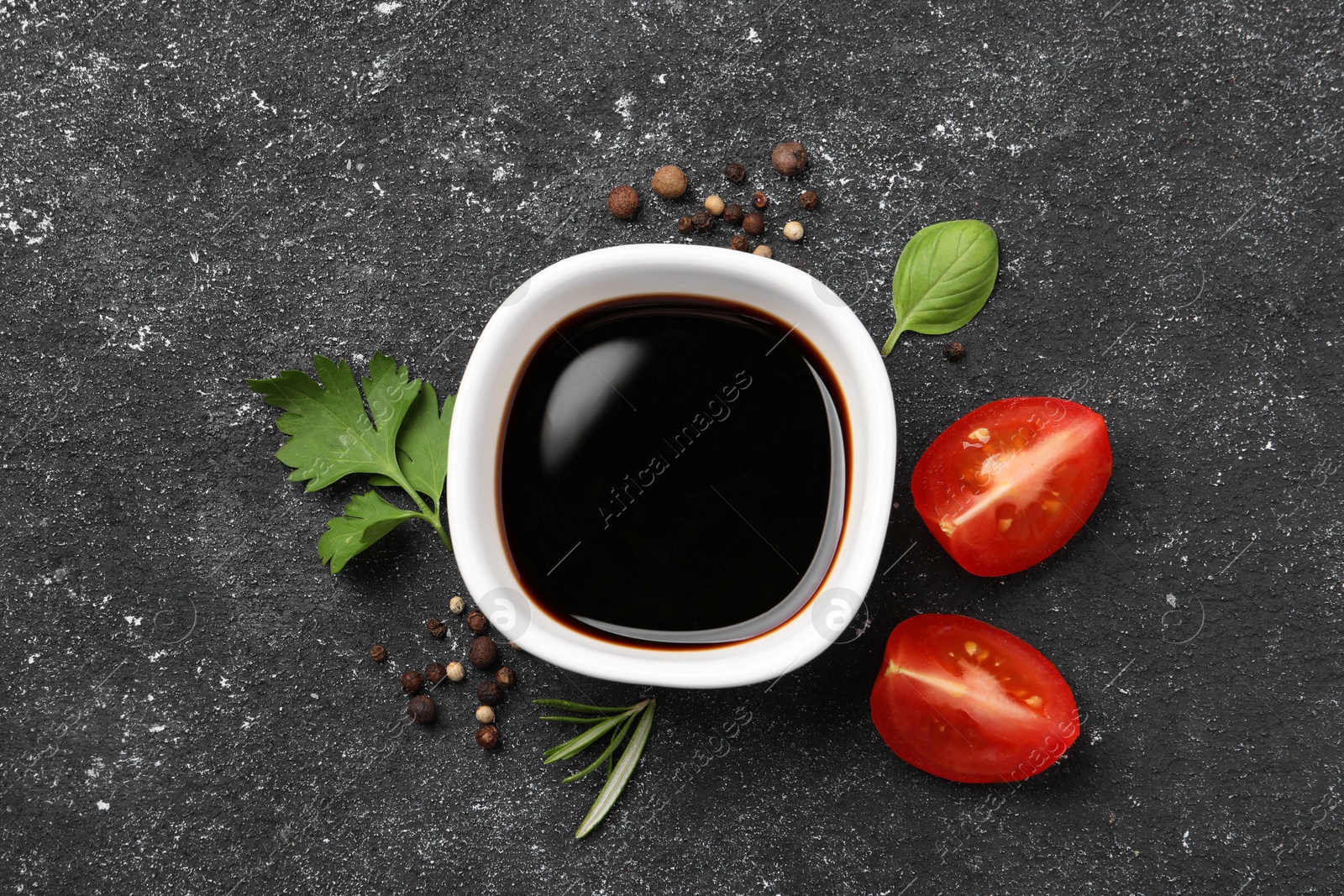 Photo of Balsamic vinegar, tomato and other products on black textured table, flat lay