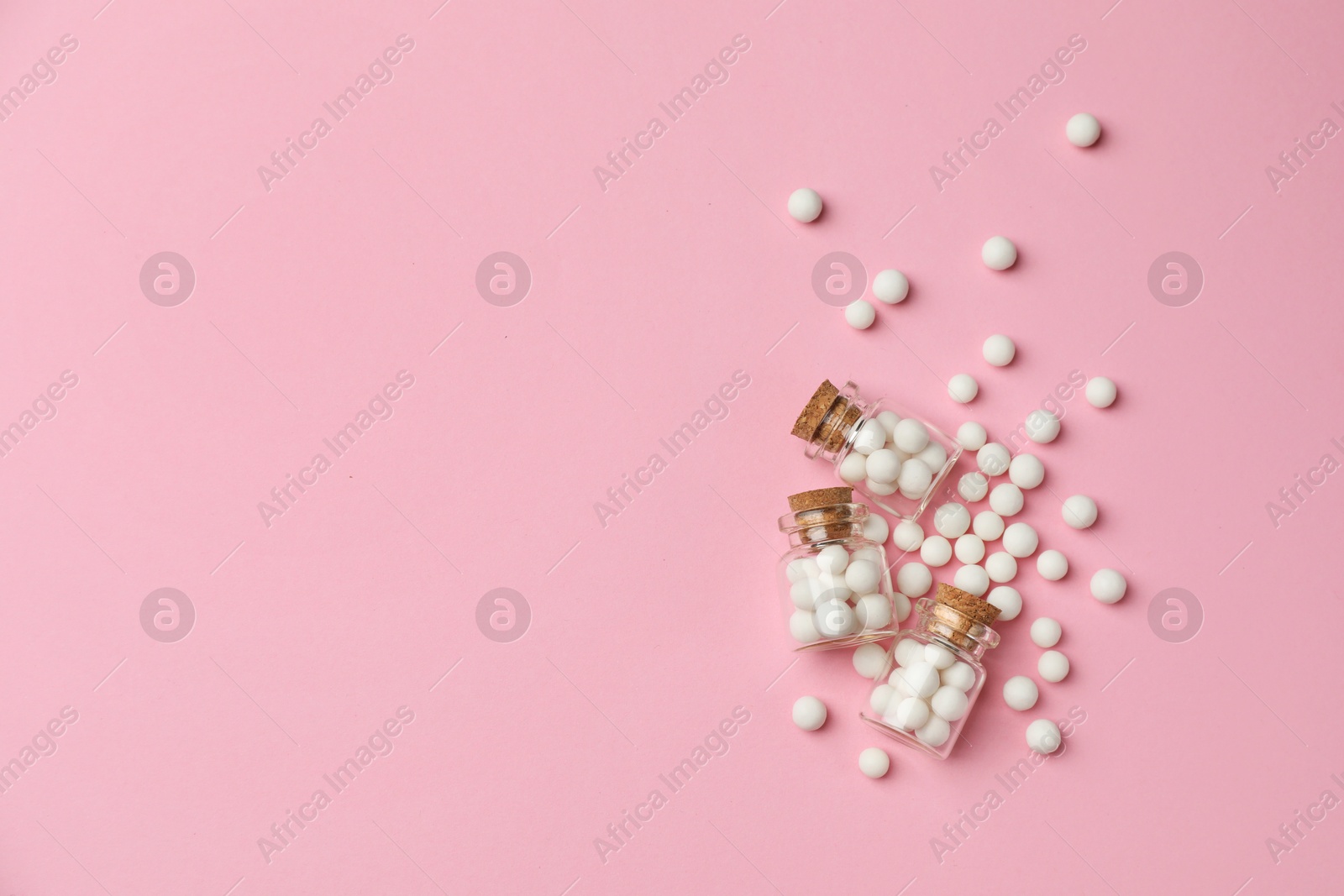 Photo of Homeopathic remedy. Glass bottles and pills on pink background, flat lay. Space for text