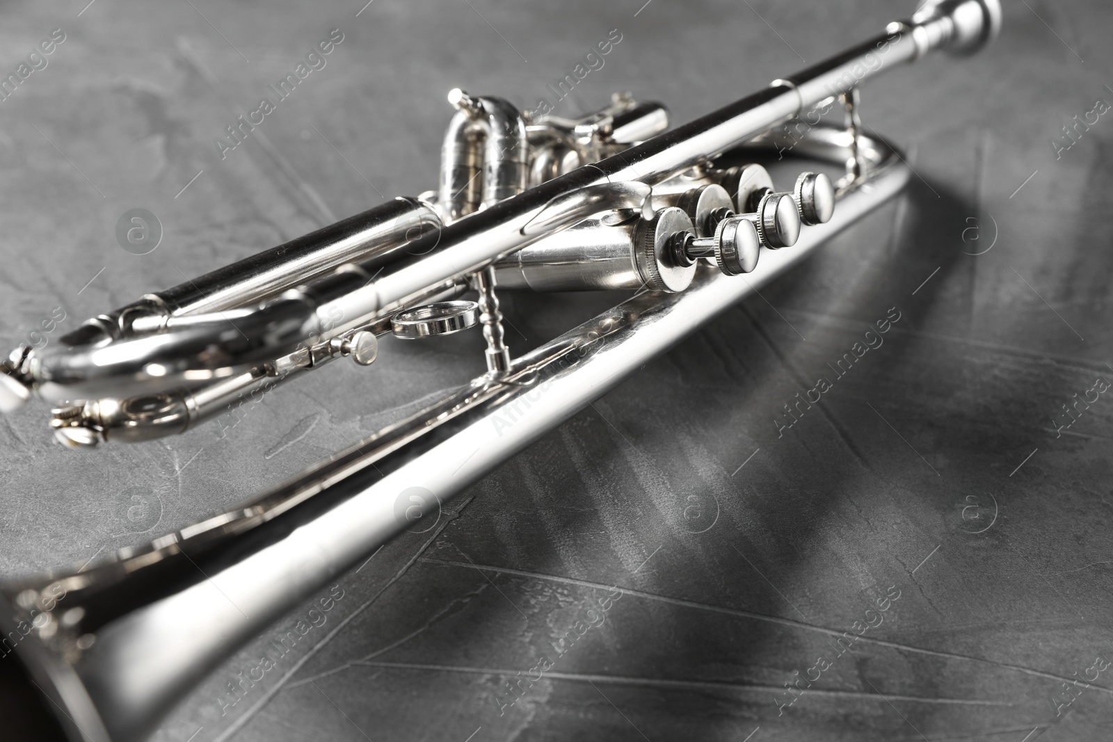 Photo of Closeup view of shiny trumpet on grey textured table. Wind musical instrument