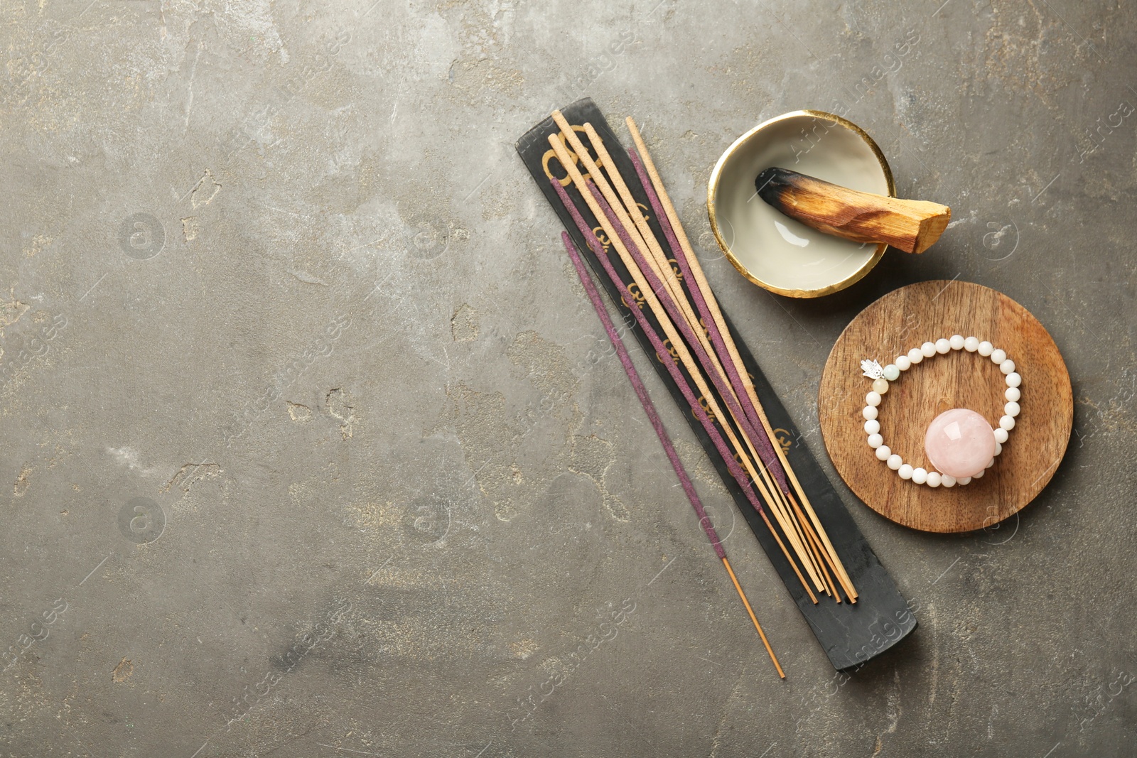 Photo of Incense sticks, holder, Santo Palo and bracelet on gray textured table, flat lay with space for text. Om ligature