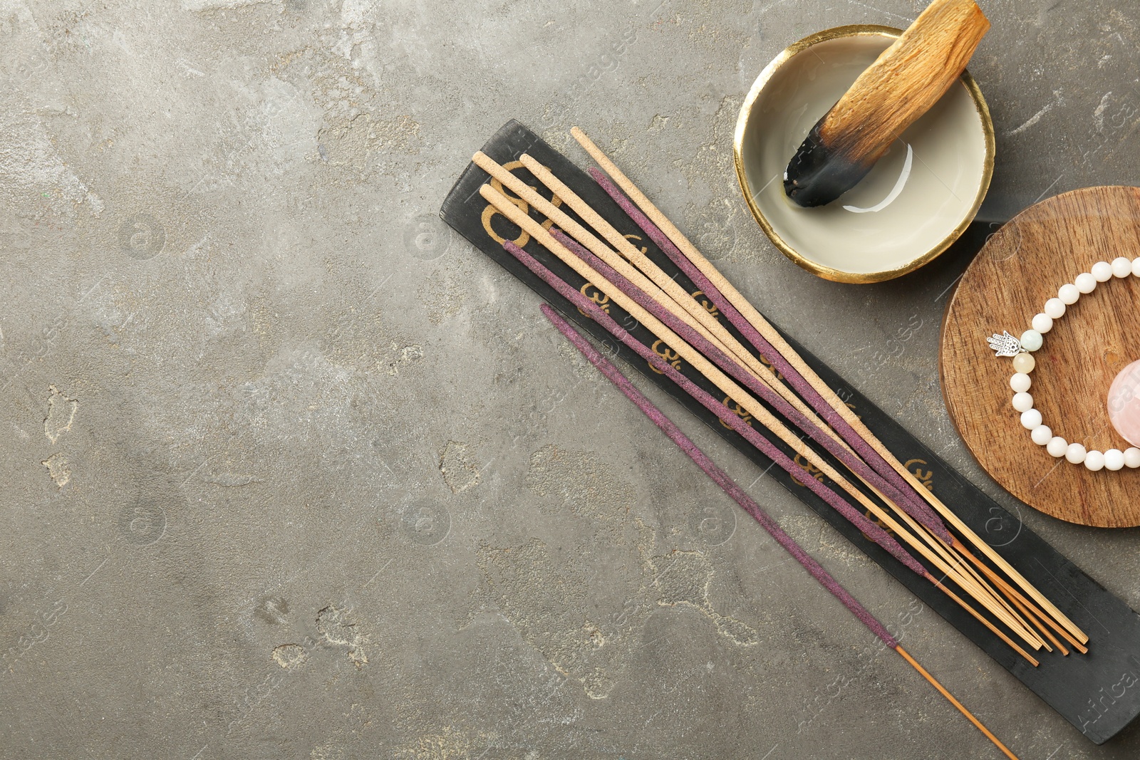 Photo of Incense sticks, holder, Santo Palo and bracelet on gray textured table, flat lay with space for text. Om ligature