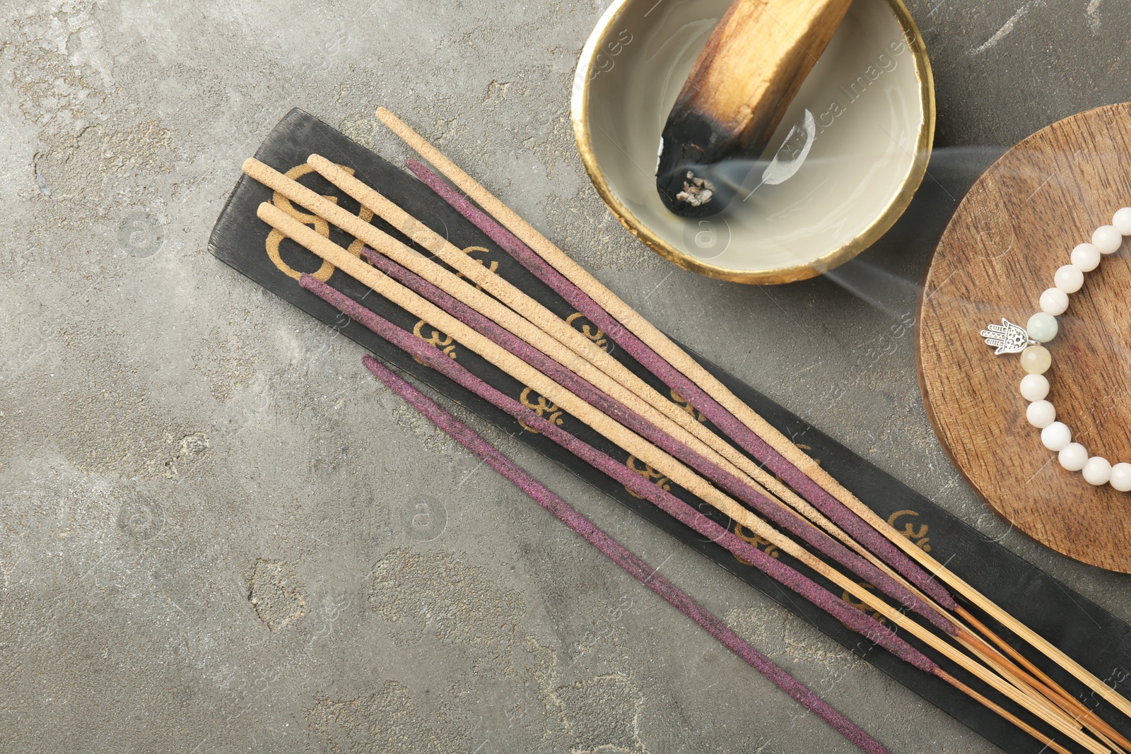 Photo of Incense sticks, holder, Santo Palo and bracelet on gray textured table, flat lay with space for text. Om ligature