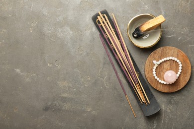 Photo of Incense sticks, holder, Santo Palo and bracelet on gray textured table, flat lay with space for text. Om ligature