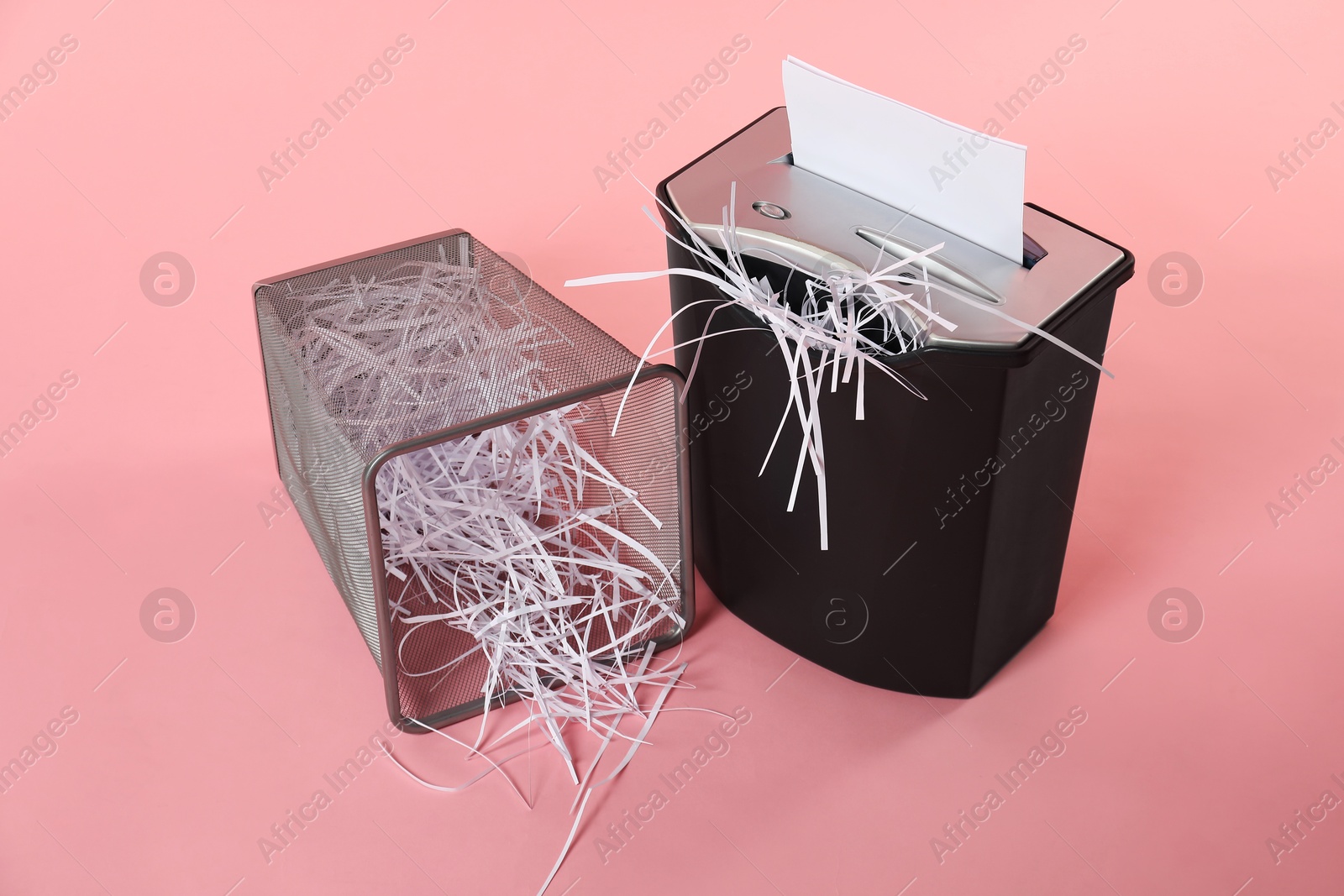 Photo of Shredder, metal basket and paper strips on pink background