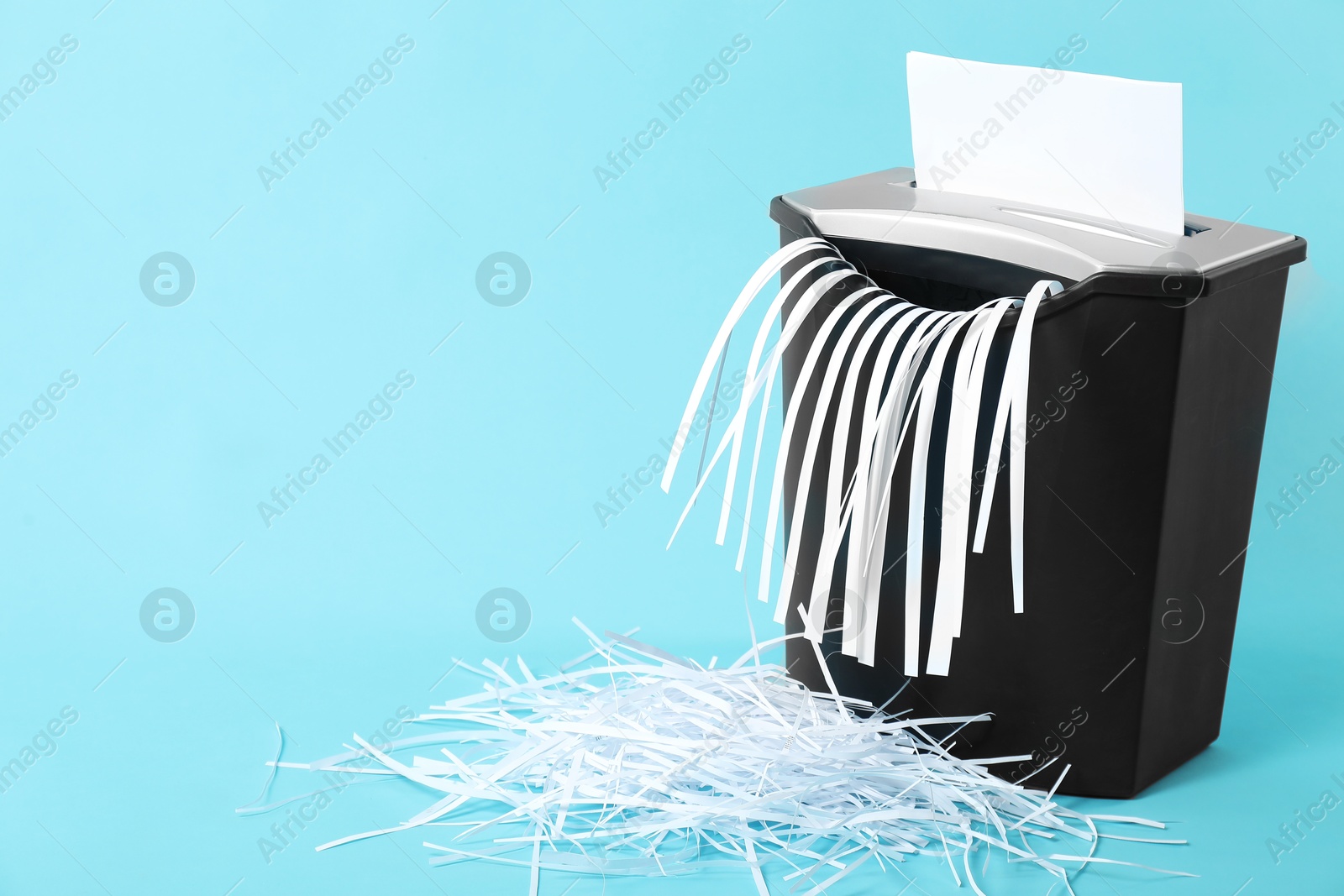 Photo of Destroying sheet of paper with shredder on light blue background, space for text