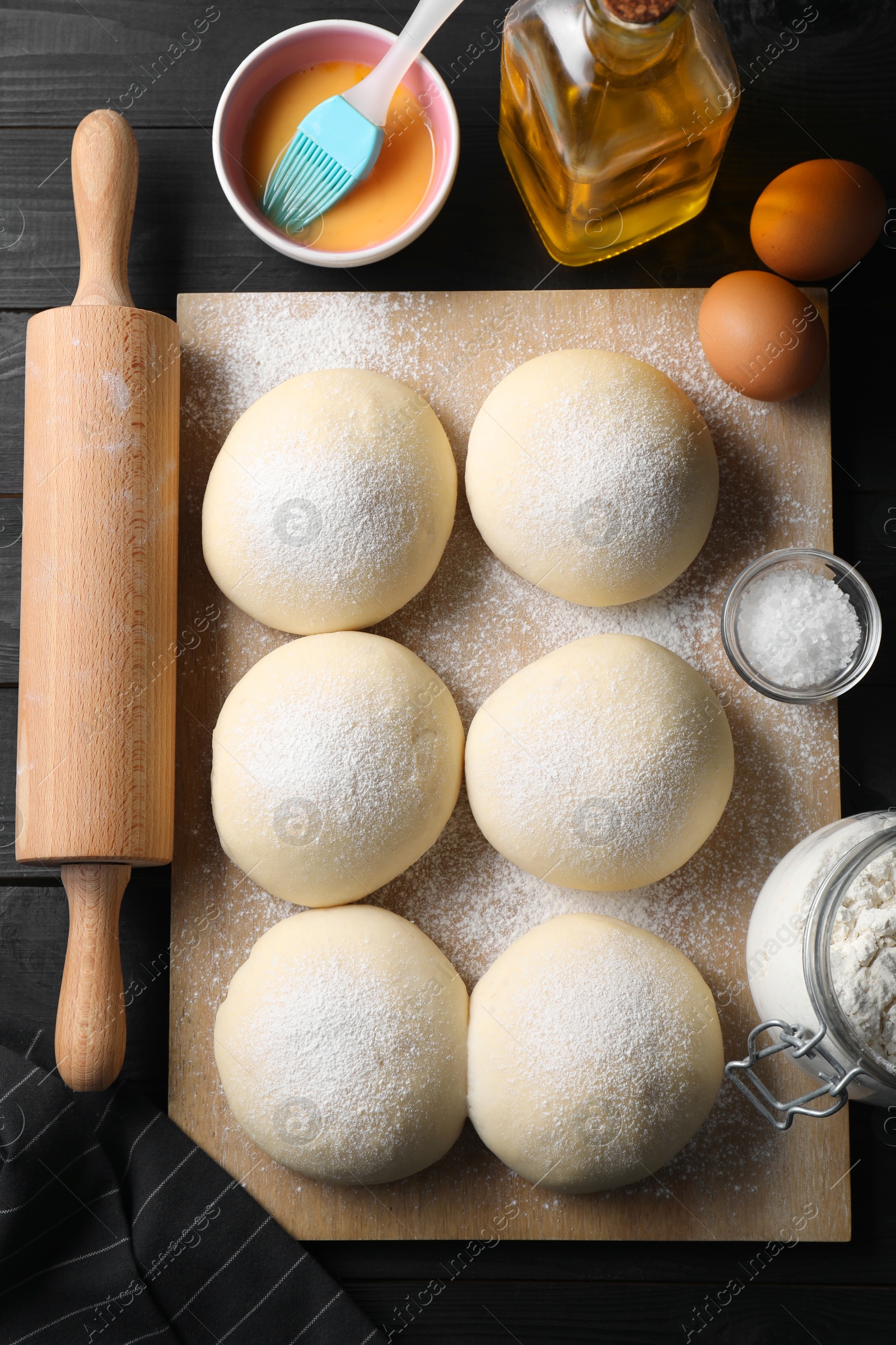 Photo of Raw dough balls, yolk, flour, eggs and rolling pin on black wooden table, top view