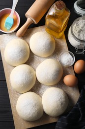 Photo of Raw dough balls, yolk, flour, eggs and rolling pin on black wooden table, top view