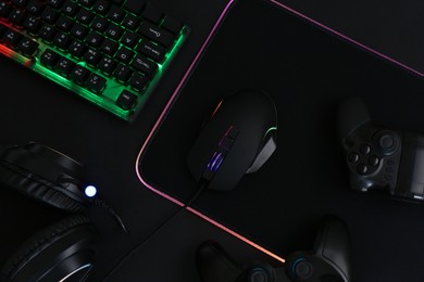 Photo of Computer mouse, RGB keyboard, game controllers and headset on black background, top view