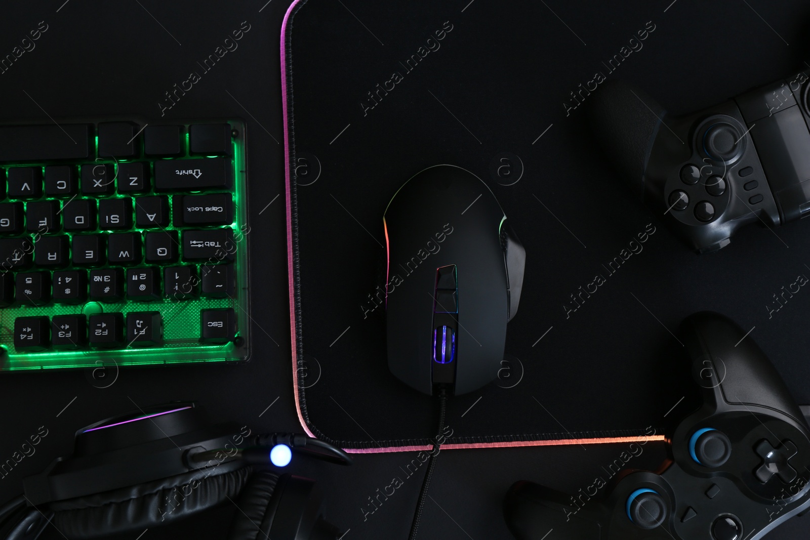 Photo of Computer mouse, RGB keyboard, game controllers and headset on black background, top view