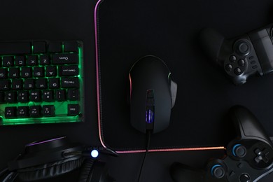 Photo of Computer mouse, RGB keyboard, game controllers and headset on black background, top view