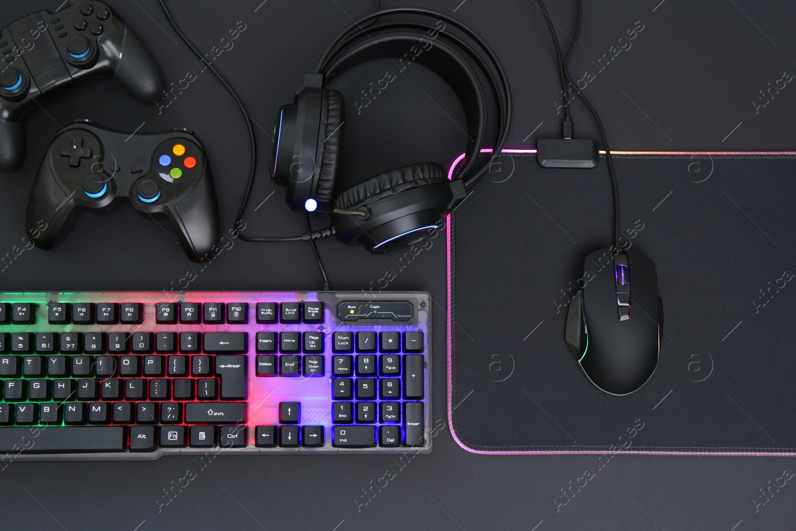 Photo of Computer mouse, RGB keyboard, headset and game controllers on black background, top view