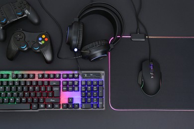 Photo of Computer mouse, RGB keyboard, headset and game controllers on black background, top view