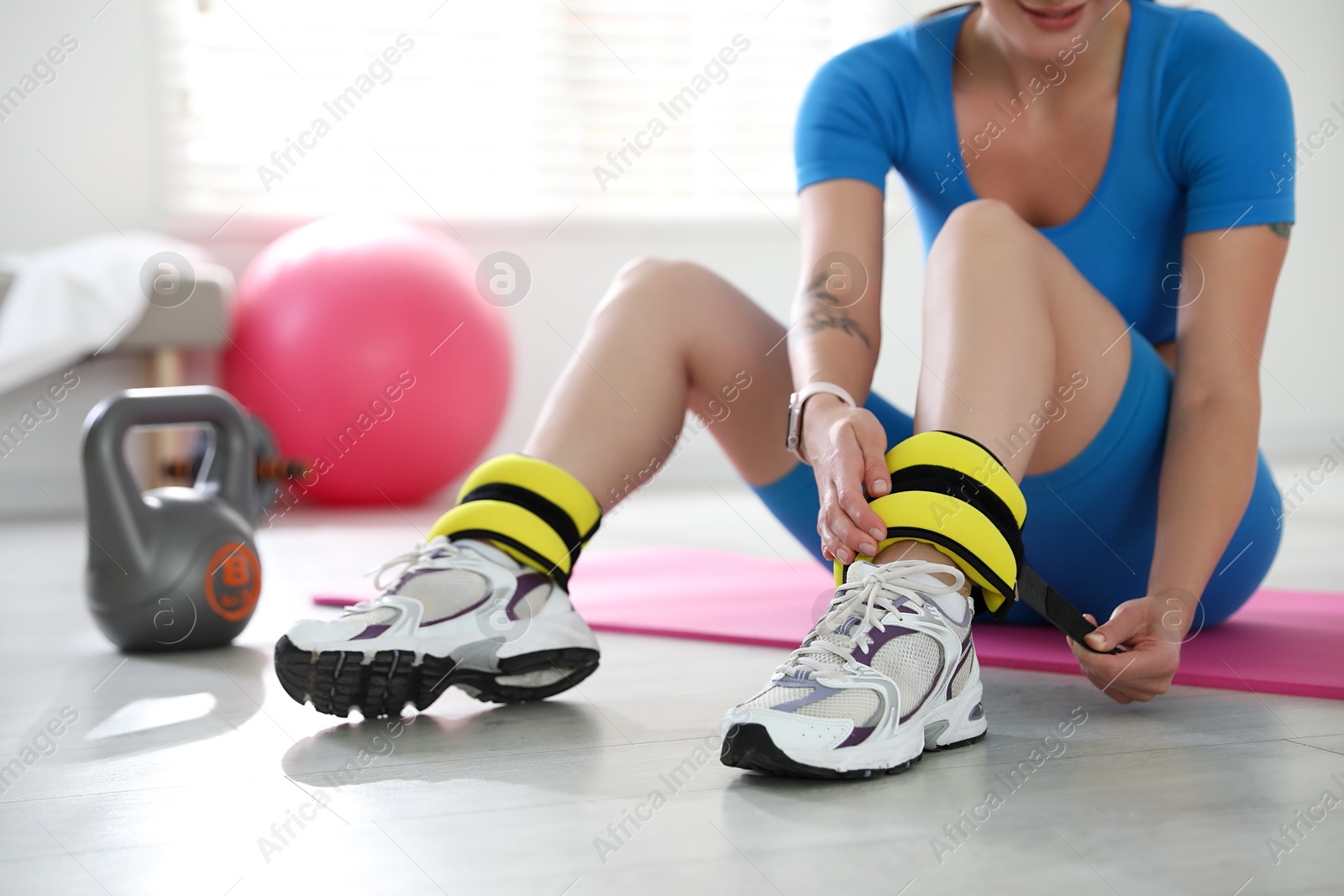 Photo of Woman putting on ankle weights indoors, closeup